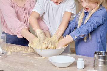 Obraz na płótnie Canvas Beautiful cute blond children help mom in the kitchen and mix the dough together