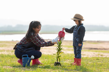 Asian  kid daughter helping mother water the plant and sapling tree outdoors in nature spring