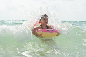 A little girl in a swimming circle is swimming in the sea. The child has fun on vacation. Sea foam and wave splashes