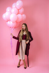 stylish young girl in burgundy clothes and pink balloons on a pink background