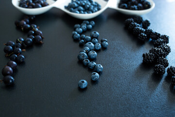 Set of different types of black berries in a white plate on a black table. Stylish seasonal vitamins