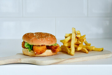Home made  spicy crispy chicken burger and french fries on wooden table isolated on dark background.