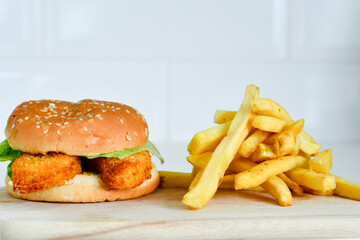Home made  spicy crispy chicken burger and french fries on wooden table isolated on dark background.
