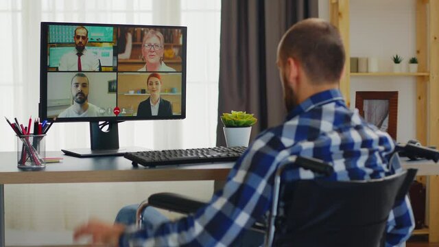 Invalid man in wheelchair greeting people during a video call working from home. Handicapped invalid paralysed freelancer, immobilized entrepreneur working from home, ilness and disability