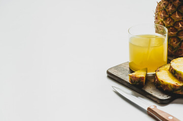 fresh pineapple juice in glass near cut delicious fruit on wooden cutting board with knife on white background