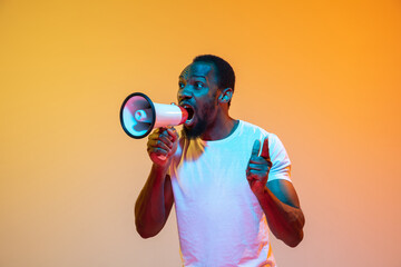 Shouting with megaphone. African-american man's modern portrait on gradient orange studio background in neon. Beautiful afro model. Concept of human emotions, facial expression, sales, ad. Copyspace.