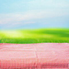 Red checked tablecloth on blur green courtyard and sky background.Summer and picnic concepts.