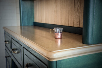 Glass in a copper cup holder on the  top of  vintage green and light brown wooden dresser