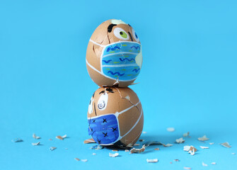Broken Easter eggs like human faces with protective masks and broken egg shells on a blue...