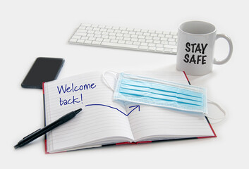 Welcome back to work concept. Medical protection mask waiting at the desk along with note pad, computer keyboard, phone, pencil and a coffee mug. Ready to work after the Coronavirus  Covid-19 pandemic