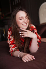 Happy young woman. Relaxed woman lying on a brown bed. Woman in retro style room in red dress