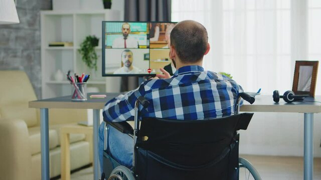 Freelancer in wheelchair waving during a business video call while working from home office. Handicapped invalid paralysed freelancer, immobilized entrepreneur working from home, ilness and disability