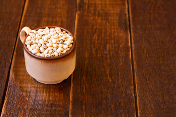 Many grains of brown raw beans in cup on wooden table. Top view with copy space