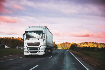 Truck Prime Mover In Motion On Summer Road Freeway. Tractor Unit On Asphalt Motorway Highway During Sunset. Traction Unit And Pink Dramatic Sunrise Sky. Business Transportation And Trucking Industry