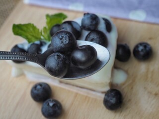 Selective focus, blueberries on wooden spoon. Piece of cheesecake with blueberry sauce on wooden board  