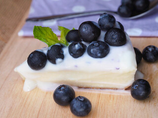 Piece of cheesecake with blueberry sauce on wooden board.