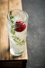 Gin based cocktail with cherries and thyme herbs on the rustic background. Selective focus. Shallow depth of field. 