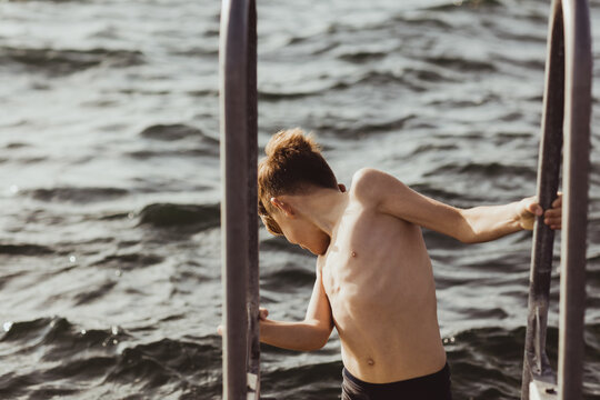 Shirtless boy moving down on ladder against sea