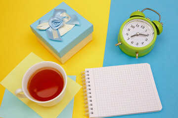 Morning cup of tea, an old-style alarm clock, a gift and copy spase notebook for wishes.