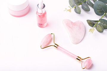 Pink hyaluronic acid serum, rose quartz roller, gua sha and moisturizing face cream on white table...