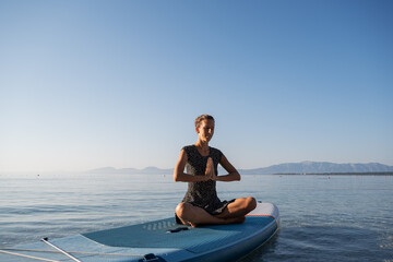 Young woman meditating on sup board floating on sea water