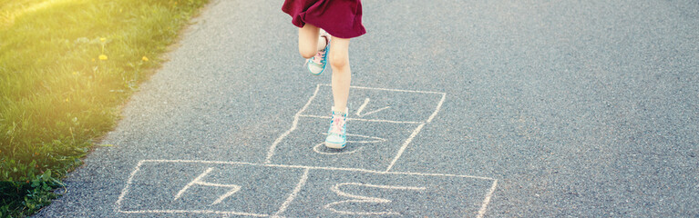 Child girl legs playing jumping hopscotch outdoors. Funny activity game for kids on playground. Summer backyard street sport for children. Happy childhood lifestyle. Header banner for website.