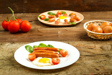 Breakfast a plate with fried egg with sausages and tomatoes on a wooden table.
