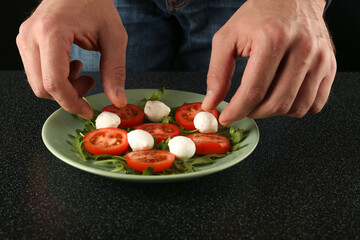man's hand cooking salad of tomatoes, herbs and mozzarella on a plate