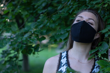 Pretty young blonde woman in medical black face mask. in a bush, forest. covid-19 concept. modern reality. copy space. High quality photo