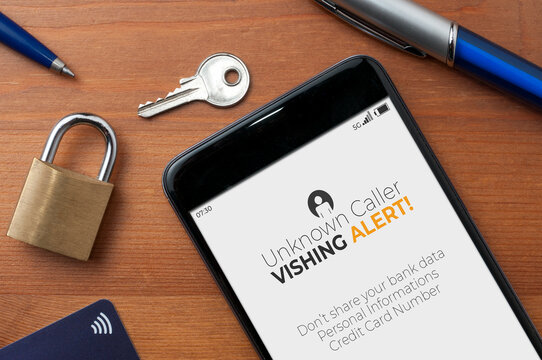 Vishing (voice phishing) concept, a smartphone on a table show an unknown caller call with vishing alert and a reminder to not share bank data, personal informations and credit card number