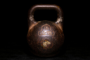 Naklejka na ściany i meble An old Soviet kettlebell weighing sixteen kilograms on a black background, in a low key. Weightlifting is a sport of the powerful. One pood of iron. Iron for physical activity.