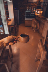 Café en vaso de barro dentro de una cafetería solo con mano