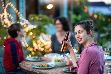 in the evening, dinner with friends around a table in the garden, in front of the wooden house. A beautiful young woman is looking at camera