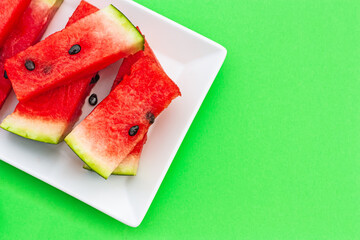 Summer creative watermelon layout. Sweet red slices of  ripe watermelon on white plate on green background. Healthy food summertime concept. Top view. Copy space