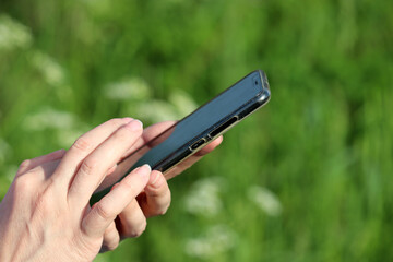 Woman using smartphone on a summer meadow. Close up of female hands with mobile phone on green nature background, concept of sms, online addiction, social media