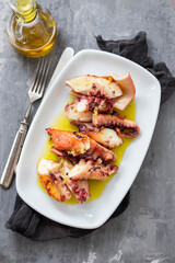 grilled octopus with olive oil on white dish on ceramic background