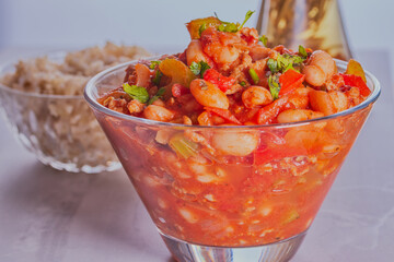 Homemade minced beef chilli served in glass dish,there is some rice in the background.