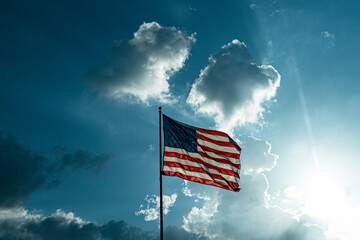 Fototapeta premium American flag on a background of blue sky with clouds.