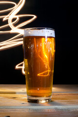 Close up Beer Glass with Light painting background. Amazing abstract colored lights in motion. Magical light in a glass of craft beer.