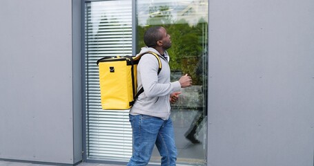 African American deliveryman with backpack over back running the street while delivering mail and looking for address. Male courier jogging outdoor.