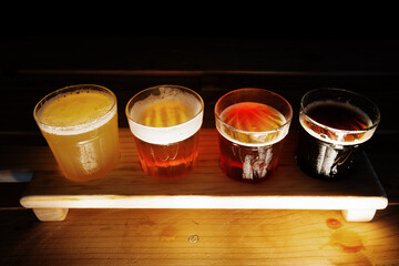 Beer samplers in small glasses individually placed in holes into a unique wooden tray and background. Amazing abstract colored lights in motion. Magical light in a glass of craft beer.