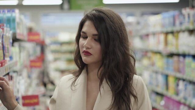 Portrait of thoughtful pretty woman examines goods on the supermarket shelves