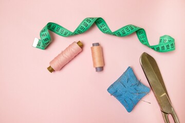 Top view of sewing machine with accessories for sewing, scissors and a measuring tape on a pink...