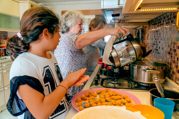 Three generation cooking: Turkish grandmother is teaching her grandchild traditional middle eastern cuisine. Girl preparing lentil balls. Elderly boiling water. Mother in kitchen background 