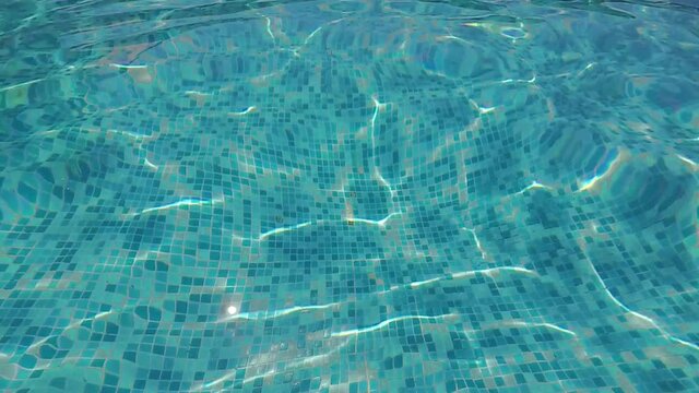 Slow motion shot of the crystal clear water shining in the pool on a sunny day with the sun glow that plays on the water