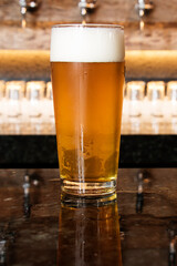 A cold glass of craft beer over a pub table with bokeh background. Happy hour time.