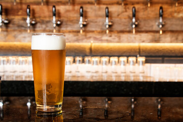 A cold glass of craft beer over a pub table with bokeh background. Happy hour time.