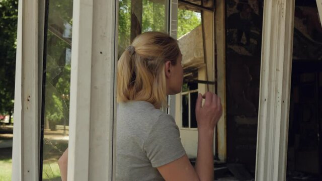 A woman enters a house destroyed by street riots through broken Windows