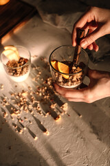 Granola and natural yogurt with slices of fruits and nuts in a glass cup in hand, healthy breakfast. Warm sunlight with shadow. Top view.