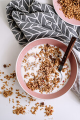 Granola muesli with fresh milk and pieces of chocolate in a pink plate on a white table. Healthly food, breakfast cooking concept.